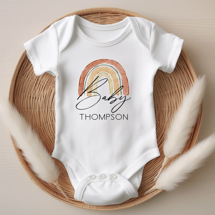 Baby announcement vests that says: Baby Thompson with a rainbow behind the text