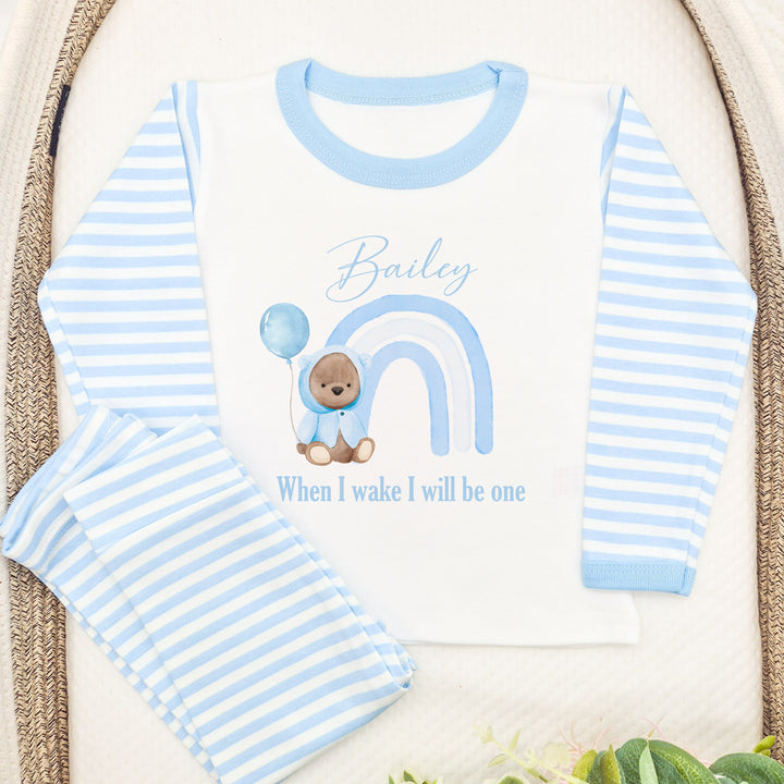 Blue Stripe birthday pyjamas that say 'Bailey When I Wake I will be one'. This design features a blue rainbow and a teddy bear wearing a blue jacket holding a balloon