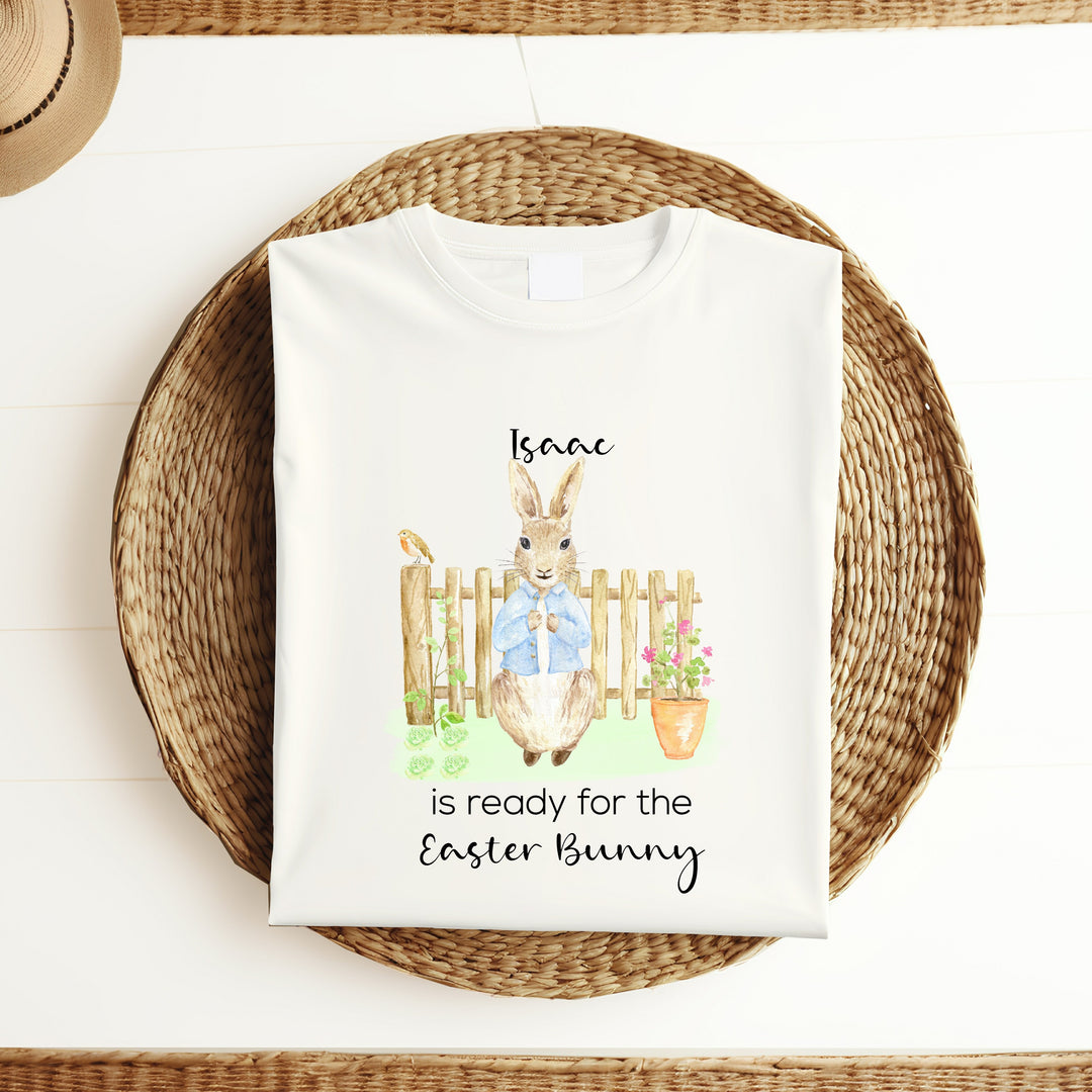 Personalised white Easter t-shirt that says 'Issac is ready fro the Easter Bunny'. This design features a rabbit wearing a blue jacket standing in front of a wooden fence