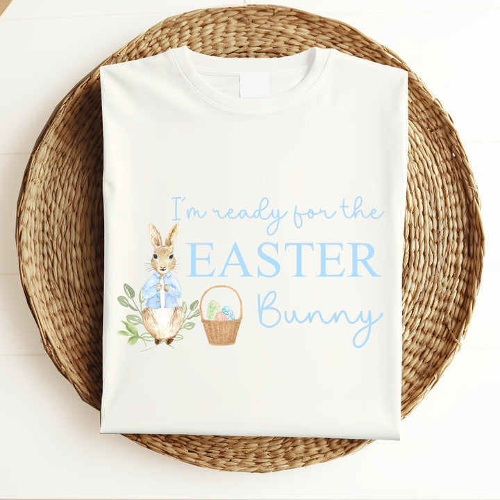 White childrens Easter t-shirt that says 'I'm ready for the Easter Bunny'. This design features a rabbit wearing a blue jacket standing next to an Easter basket full of eggs