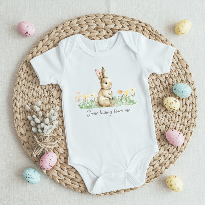 White Easter baby vest that says 'Some bunny loves me'. This design features a brown bunny sitting in flowers.