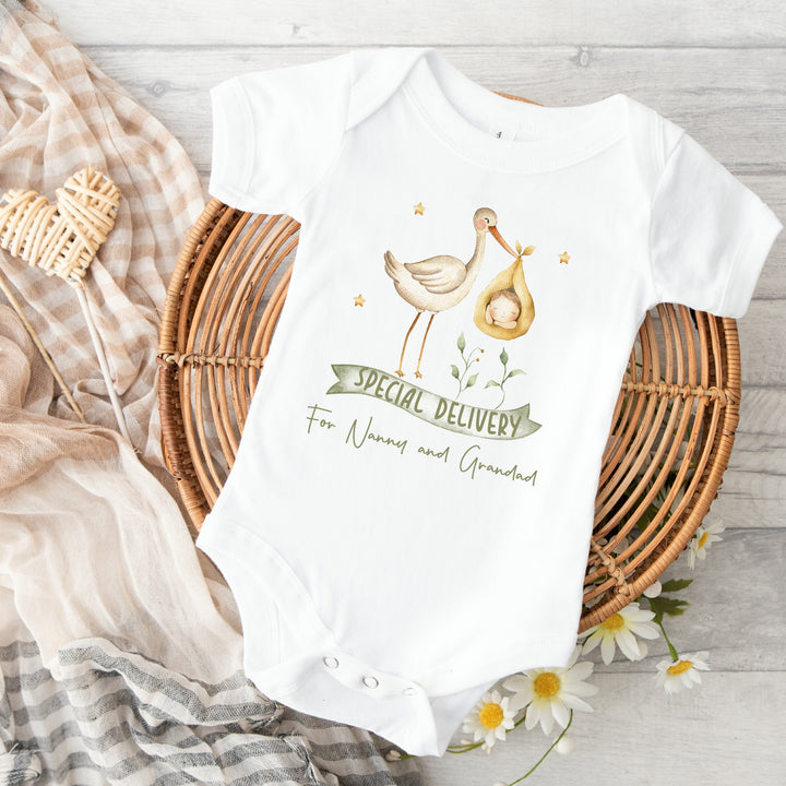 Baby announcement vests that says: 'Special Delivery For Nanny and Grandad' With a white stork carrying a baby in a yellow basket