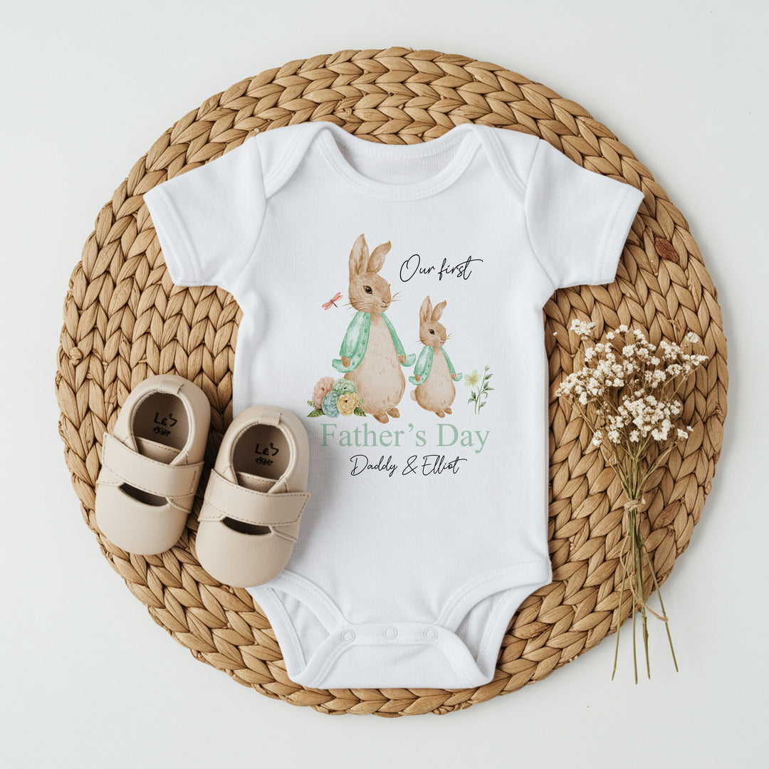 Personalised white Father's Day baby vest that says 'Our First Father's Day Daddy & Elliot'. This design features 2 rabbits wearing sage green jackets