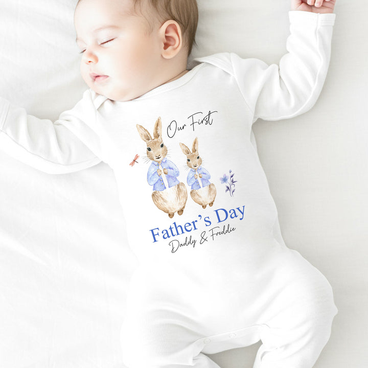 Personalised white Father's Day baby grow/sleepsuit that says 'Our First Father's Day Daddy & Freddie'. This design features 2 rabbits wearing blue jackets