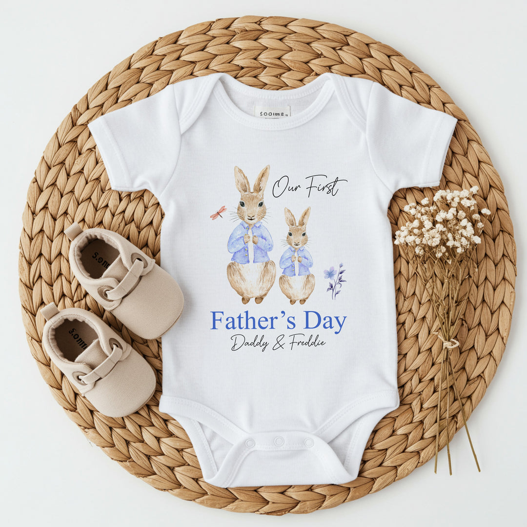 Personalised white Father's Day baby vest that says 'Our First Father's Day Daddy & Freddie'. This design features 2 rabbits wearing blue jackets