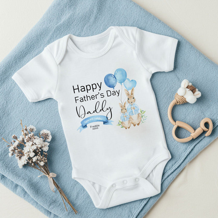 Personalised white Father's Day baby vest that says 'Happy Father's Day Daddy Love and Cuddles Freddie xoxo'. This design features 2 rabbits wearing blue jackets