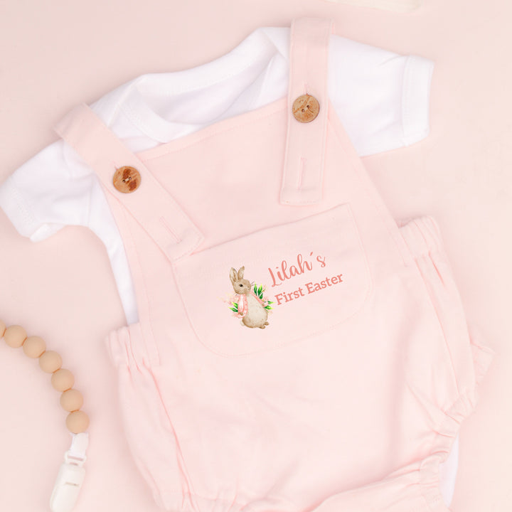 Personalised pink Easter dungarees that say 'Lilah's First Easter'. This design features a rabbit wearing a pink jacket 