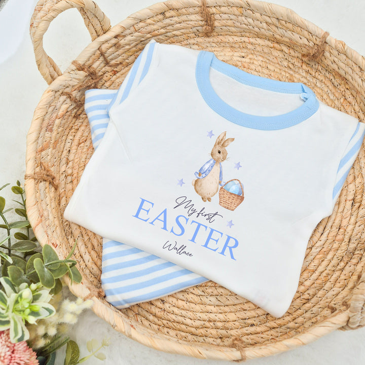 Personalised blue stripe Easter pyjamas that say 'My First Easter Wallace'. This design features a rabbit wearing a blue jacket next to a basket with Blue Easter eggs