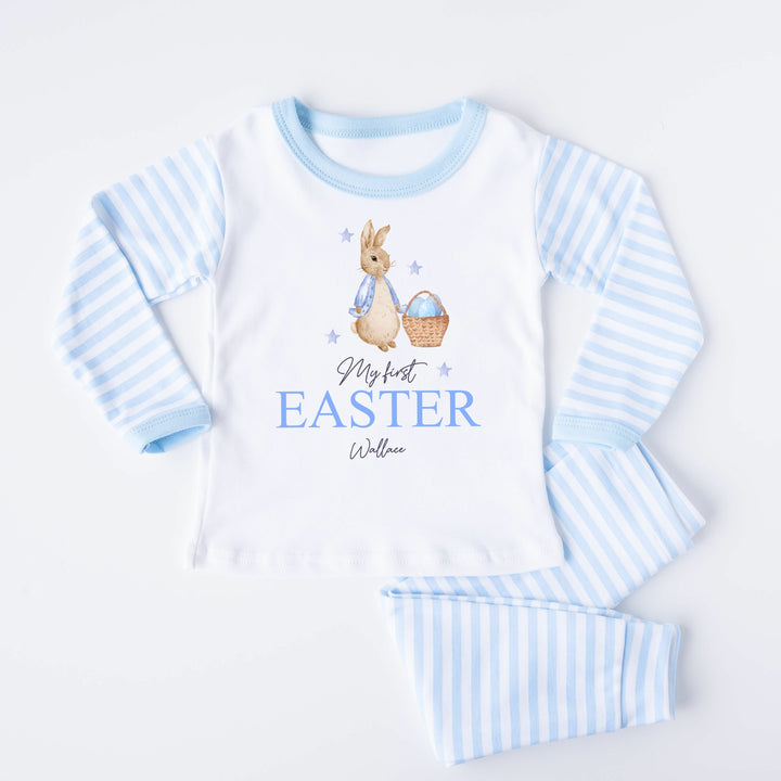 Personalised blue stripe Easter pyjamas that say 'My First Easter Wallace'. This design features a rabbit wearing a blue jacket next to a basket with Blue Easter eggs