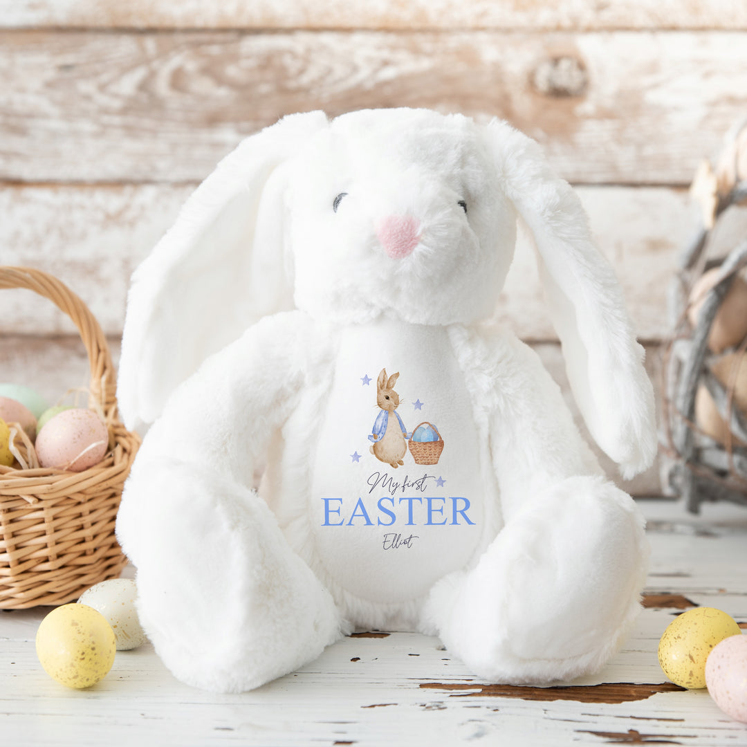 Personalised white bunny Easter teddy that says 'My First Easter Elliot'. This design features a rabbit wearing a blue jacket holding an Easter basket filled with eggs