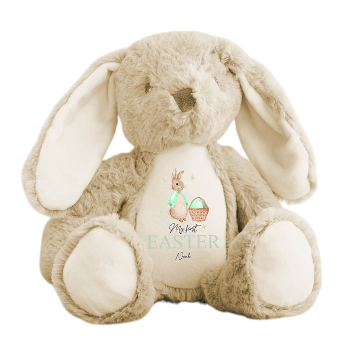 Personalised beige bunny Easter teddy that says 'My First Easter Noah'. This design features a rabbit wearing a green jacket next to a basket full of Easter eggs