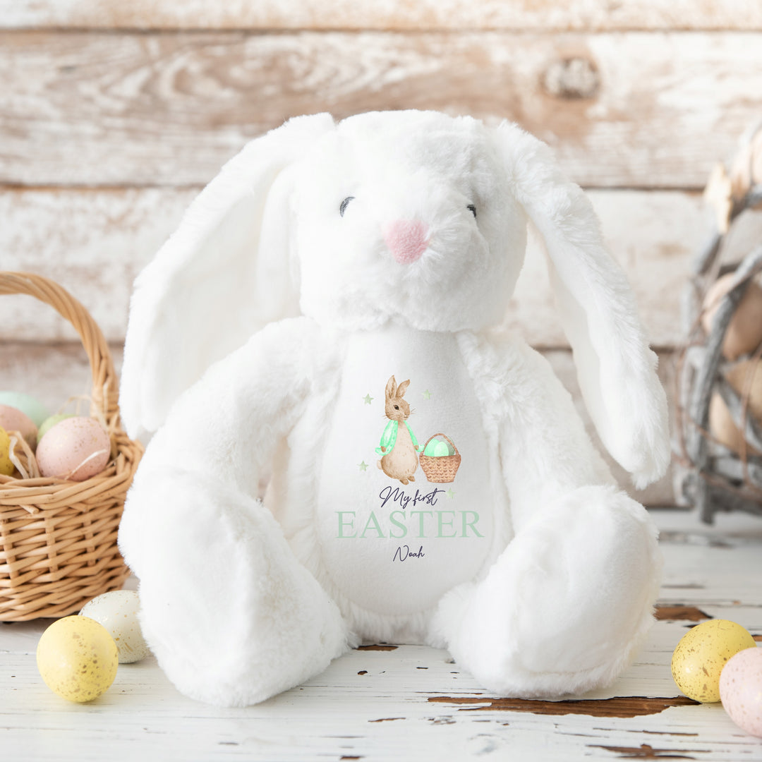 Personalised white bunny Easter teddy that says 'My First Easter Noah'. This design features a rabbit wearing a green jacket next to a basket full of Easter eggs