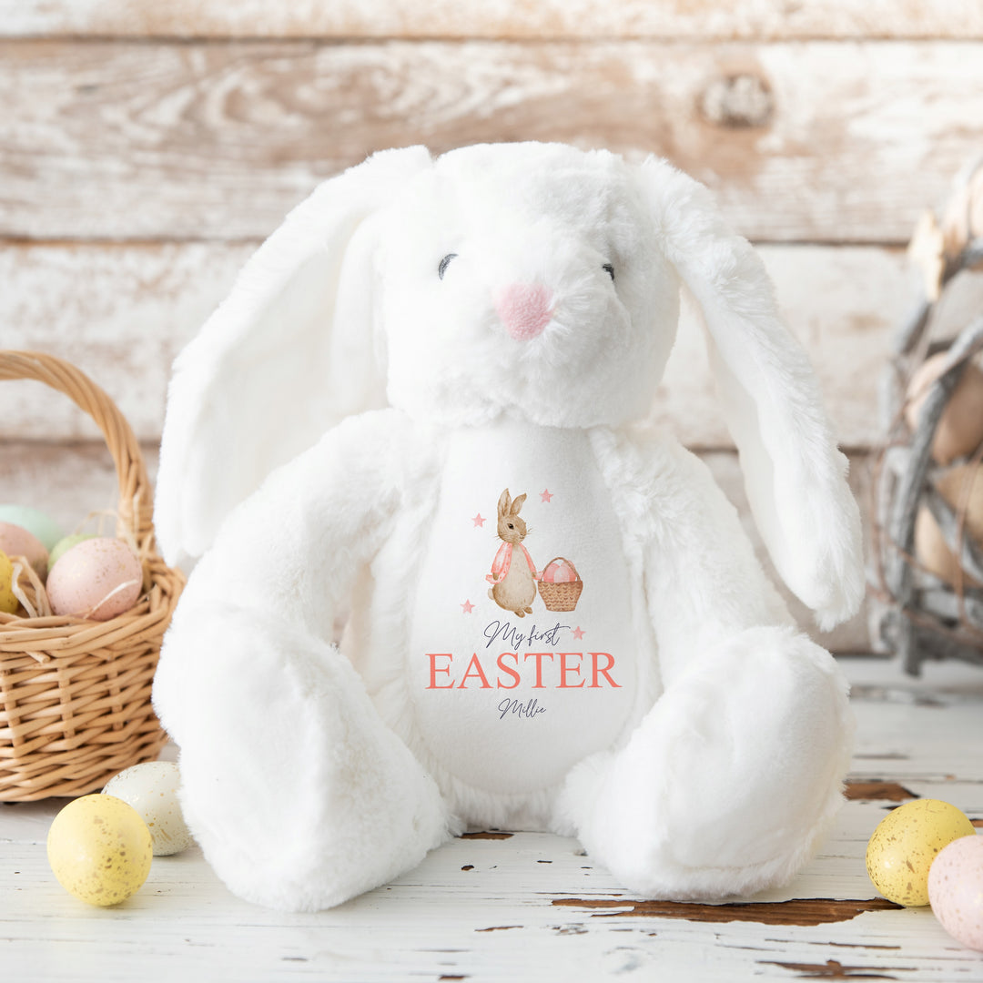 Personalised white rabbit Easter teddy that says 'My First Easter Millie'. This design features a rabbit wearing a pink jacket holding an Easter basket full of eggs