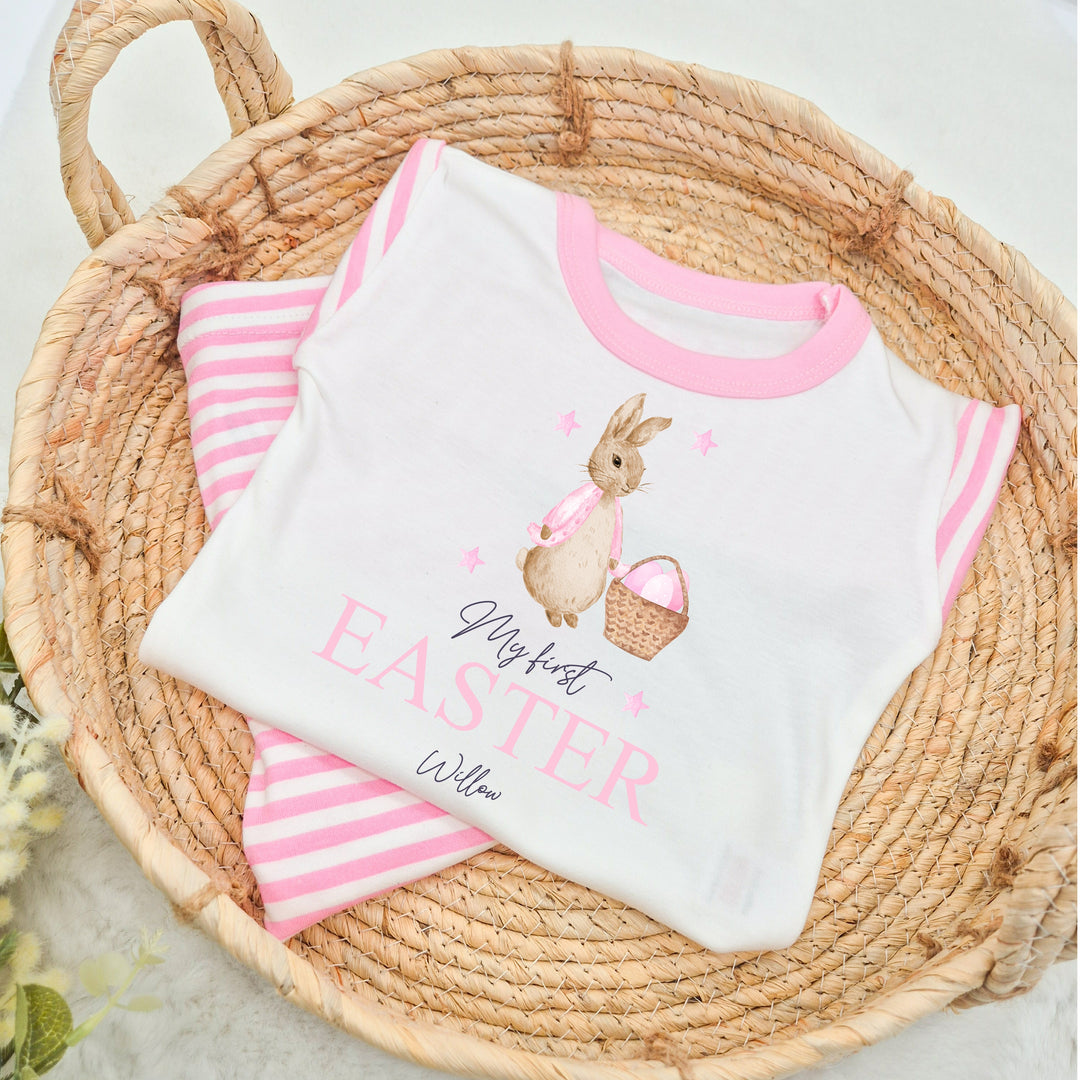 Personalised pink stripe Easter pyjamas saying 'My First Easter Willow'. This design features a rabbit wearing a pink jacket with a basket on pink easter eggs