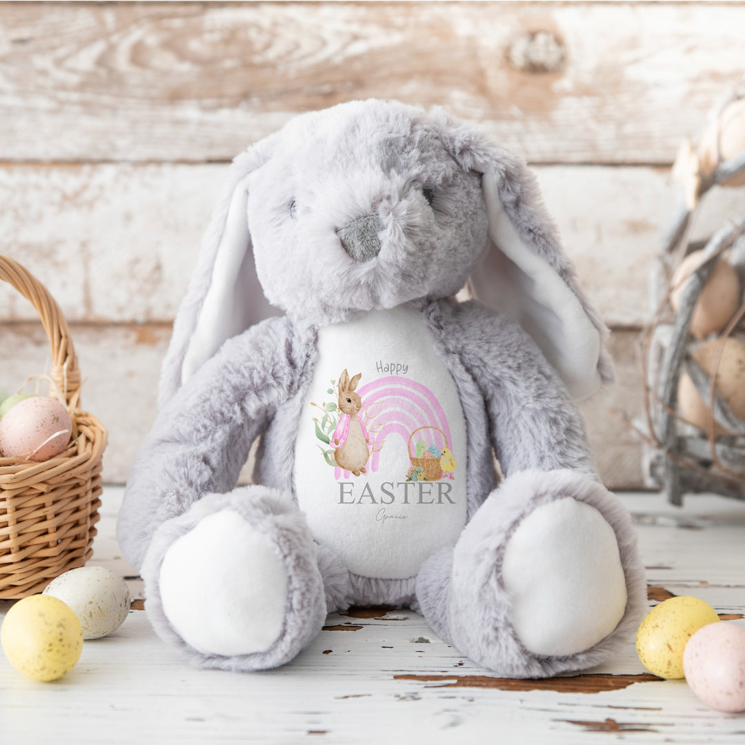 Personalised grey bunny Easter teddy that says 'Happy Easter Gracie'. This design features a pink rainbow with a rabbit wearing a pink jacket on one side and an Easter basket on the other side