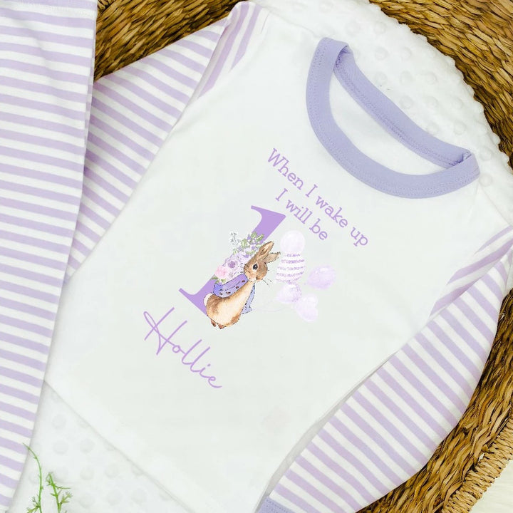 A pair of lilac and white stripe children's birthday pyjamas with a purple bunny rabbit with balloons design saying "When I wake up I will be one" with the name "Hollie".