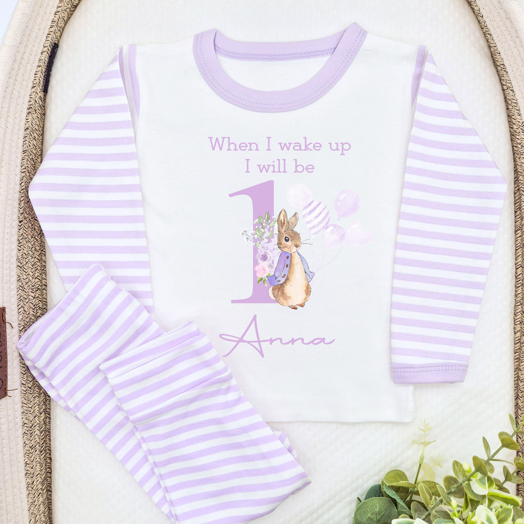 A pair of lilac and white stripe children's birthday pyjamas with a purple bunny rabbit with balloons design saying "When I wake up I will be one" with the name "Anna".