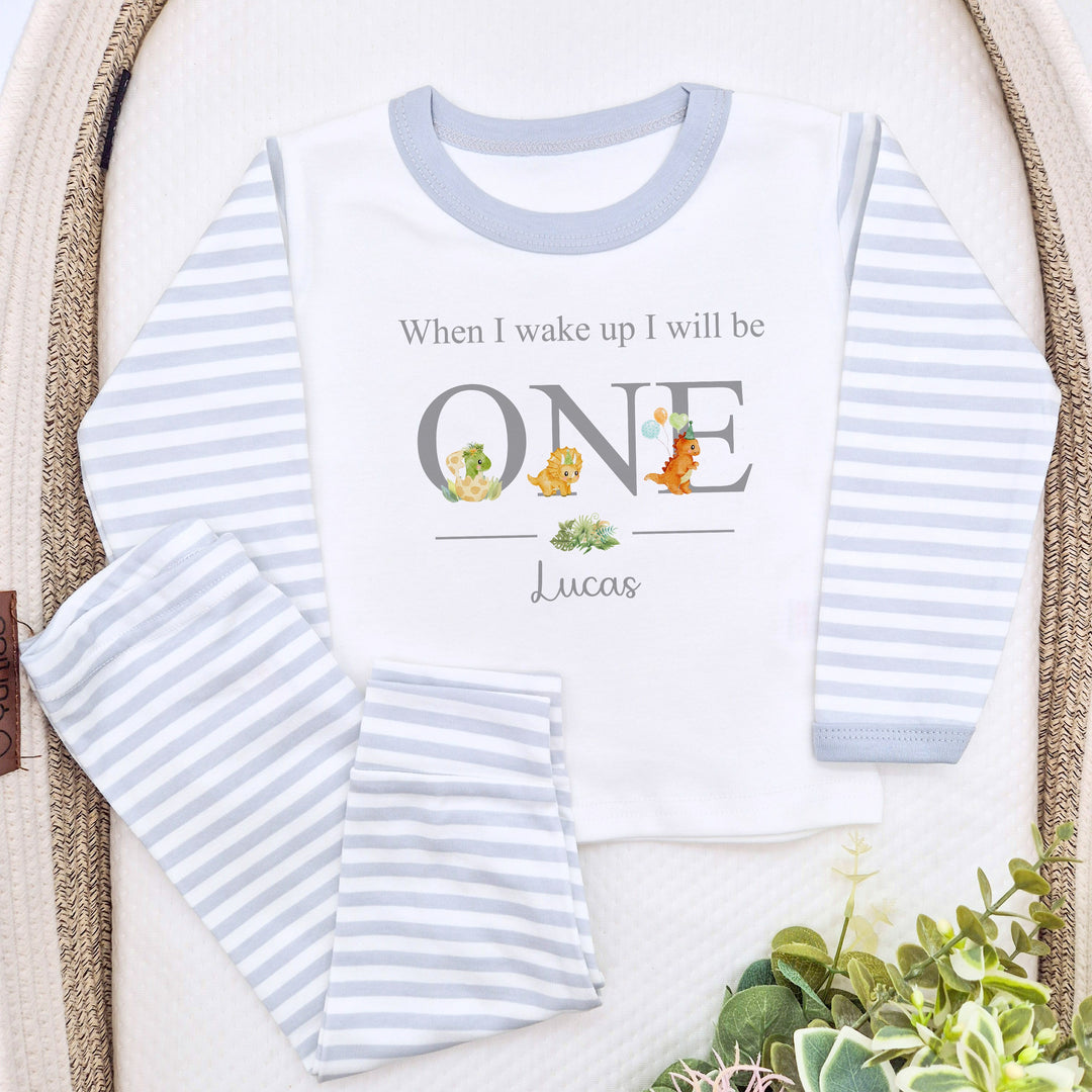 A pair of grey and white stripe children's birthday pyjamas with a dinosaur design saying "When I wake up I will be One" with the name "Lucas".