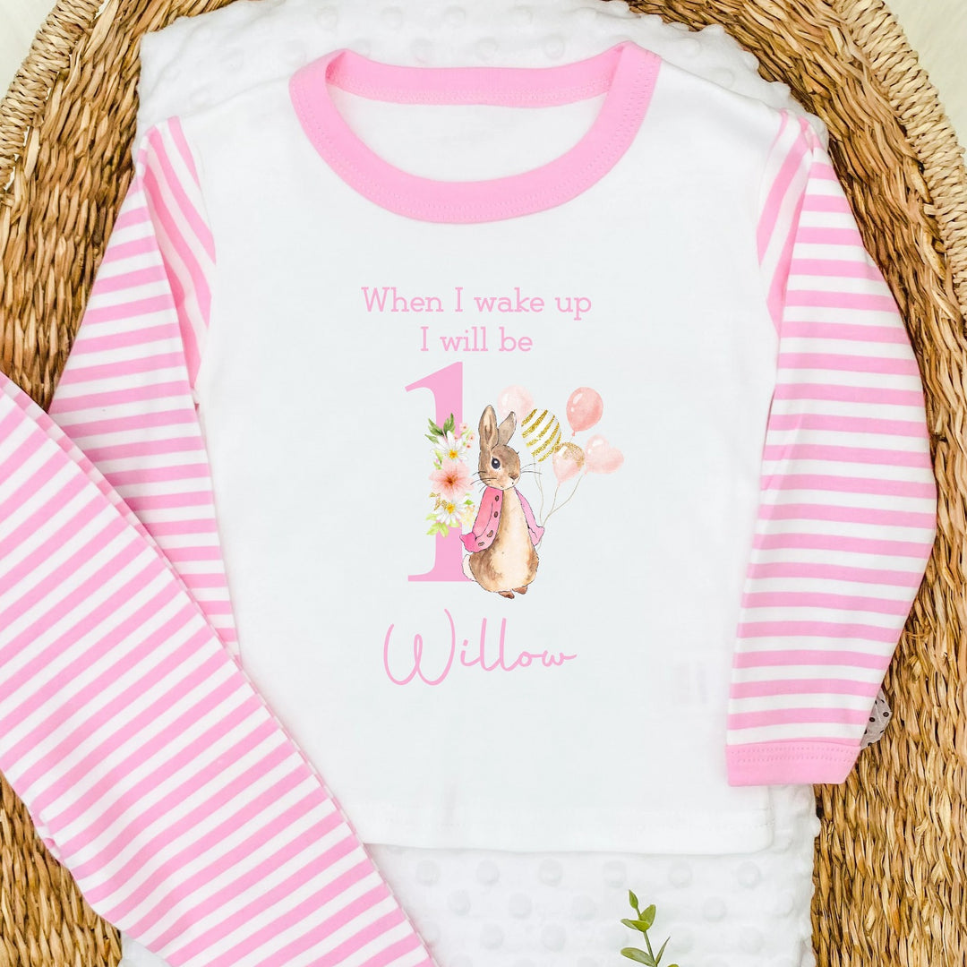 A pair of printed pink striped pyjamas. The design features a rabbit with text saying "when I wake up I will be 1". A name can be added at the bottom of the design.