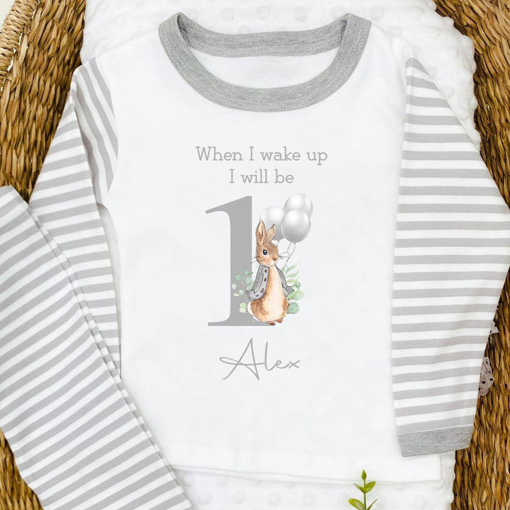 A pair of grey and white stripe children's birthday pyjamas with a grey bunny with balloons design saying "When I wake up I will be One" with the name "Alex".