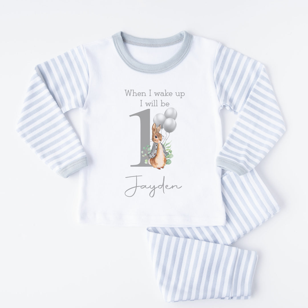 A pair of grey and white stripe children's birthday pyjamas with a grey bunny with balloons design saying "When I wake up I will be One" with the name "Jayden".