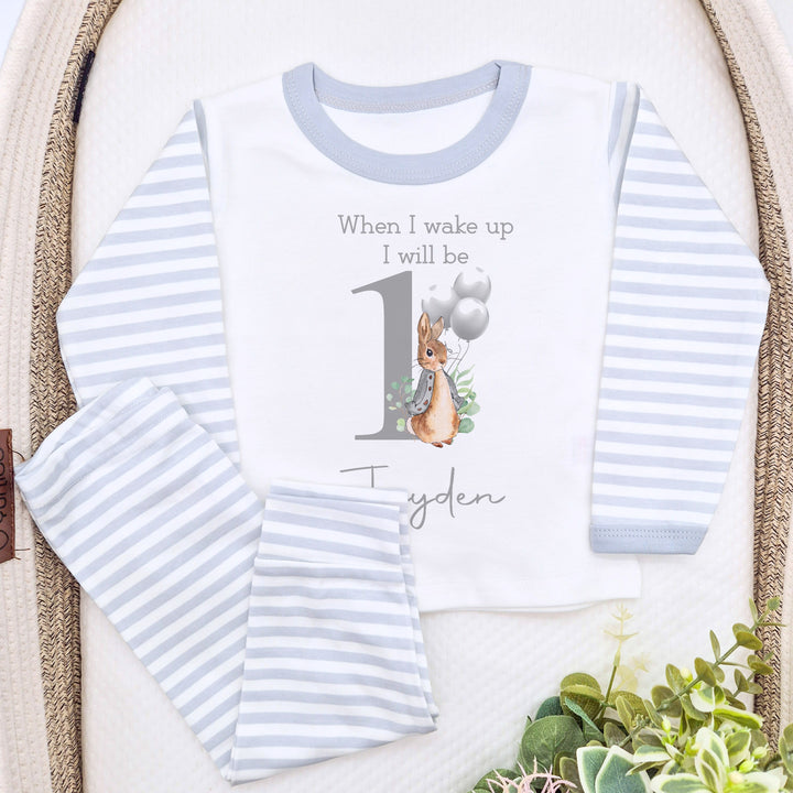 A pair of grey and white stripe children's birthday pyjamas with a grey bunny with balloons design saying "When I wake up I will be One" with the name "Alex".