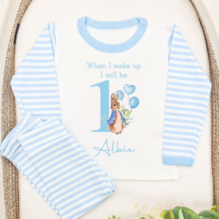 Blue Stripe pyjamas that say: When I Wake up I will be 1 Albie with a rabbit in a blue jacket holding balloons next to the number 1.