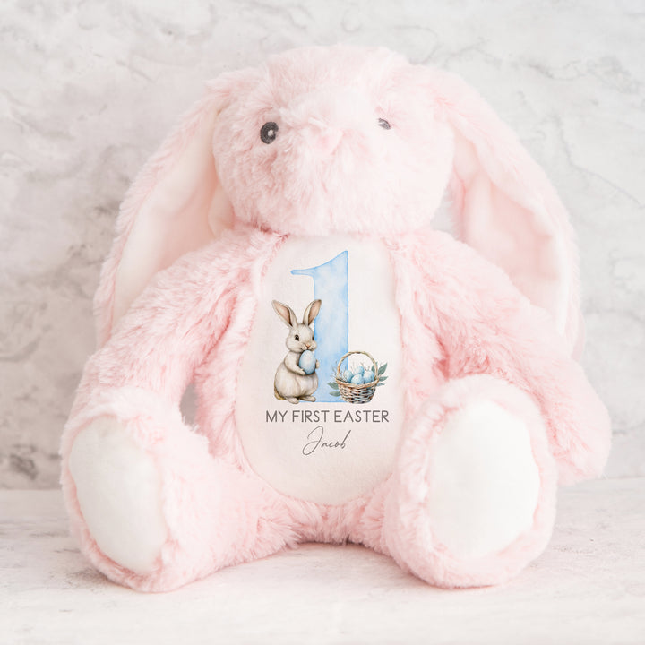 Personalised pink bunny Easter teddy that says 'My First Easter Jacob'. This design features a white bunny holding a blue Easter egg