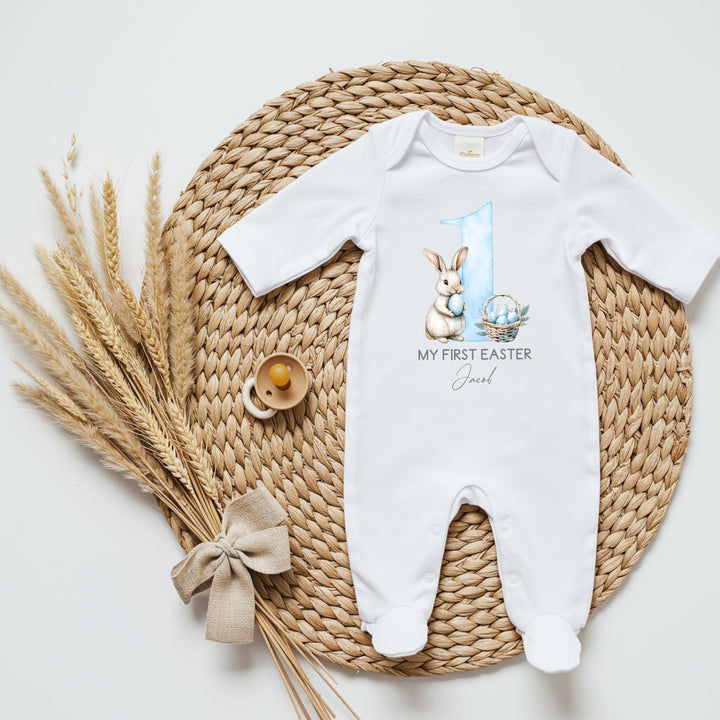 Personalised white Easter baby grow/sleepsuit that says 'My First Easter Jacob'. This design features a big blue 1 with a white bunny holding a blue Easter egg