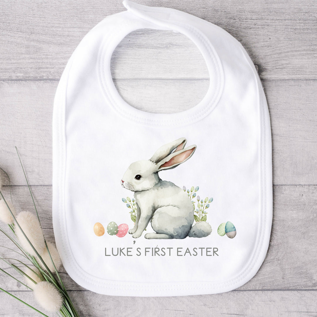 Personalised white Easter baby bib that says 'Luke's first Easter'. This design features a white bunny surrounded by Easter eggs