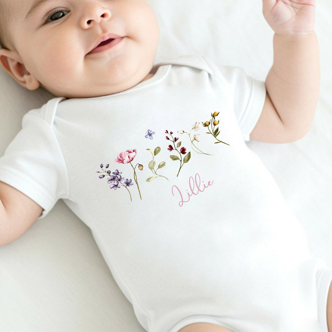 a personalised white baby vest that say 'Lillie' this design features lots of wild flowers