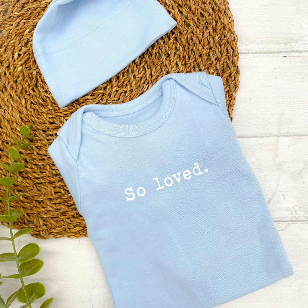 Blue babygrow and hat printed with the text "So Loved."